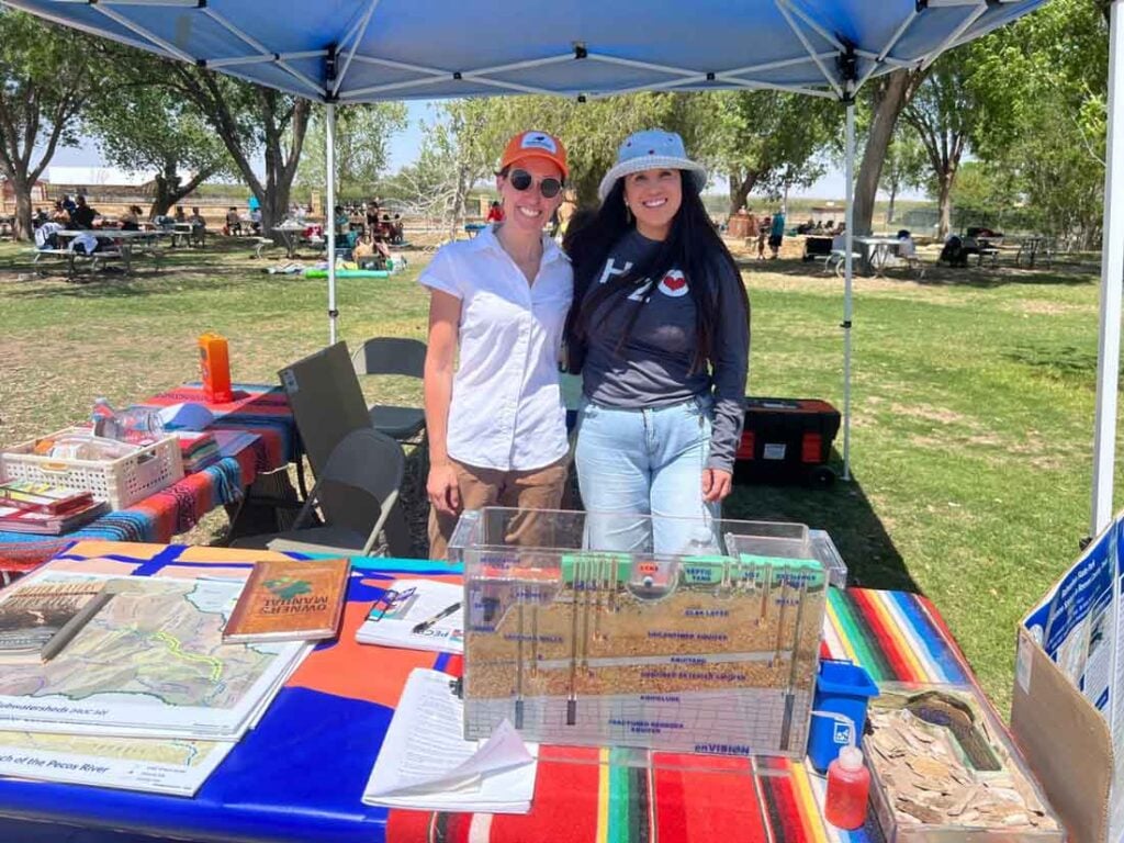 Kelbi Delaune, Ph.D. and another person at a public outreach event standing behind a table under a pop up tent.