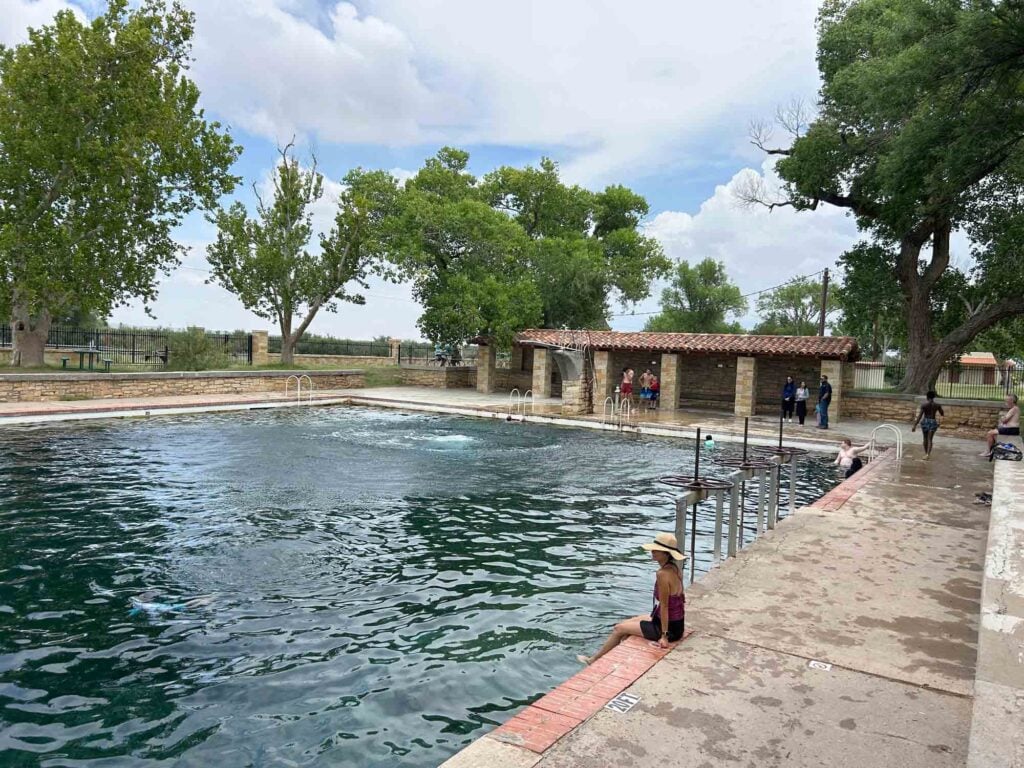 Spring fed pool water with covered patio and people in and around the pool.