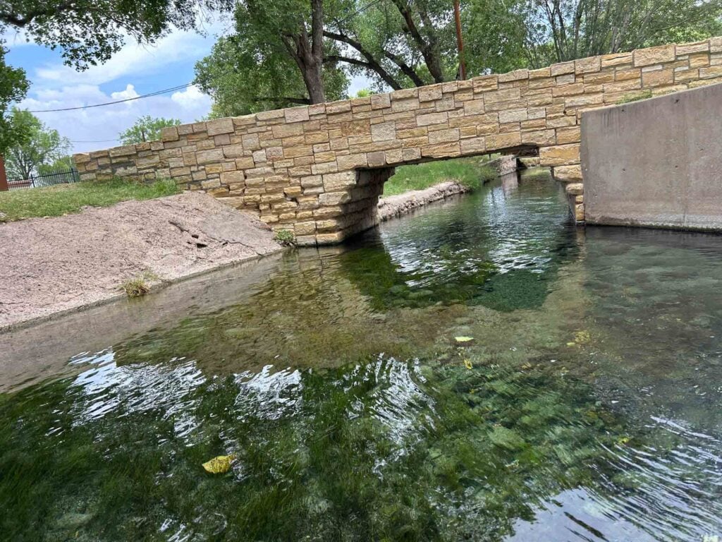 Water of San Solomon springs with retaining wall and bridge over the water.